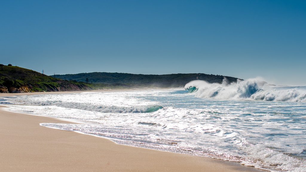 Catherine Hill Bay with its historic coal jetty stretching into the ocean, surrounded by golden sand and rolling waves, blending natural beauty with heritage charm.