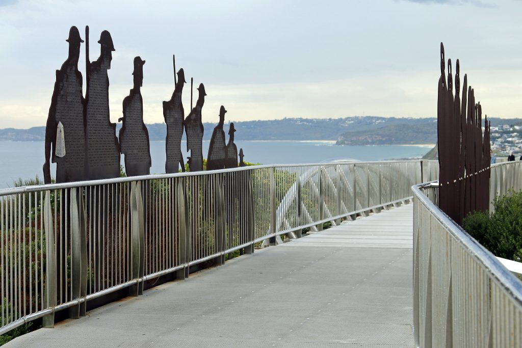 Newcastle Memorial Walk bridge above the ocean cliffs. Steel soldier silhouettes line the walkway, engraved with the names of soldiers from the region who enlisted in WW1.